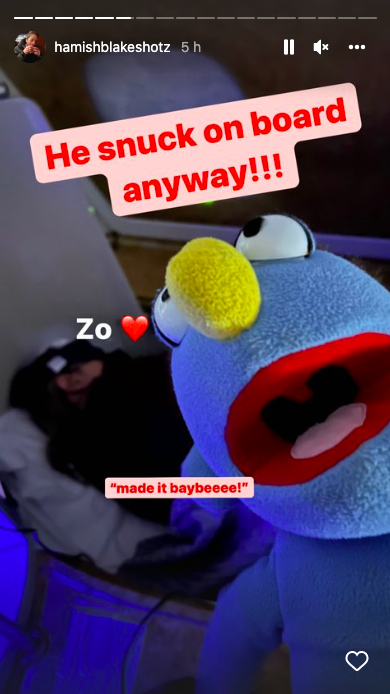 Screenshot of a blue puppet on a plane with the caption: "He snuck on board anyway!!!" shared by Hamish Blake on Instagram