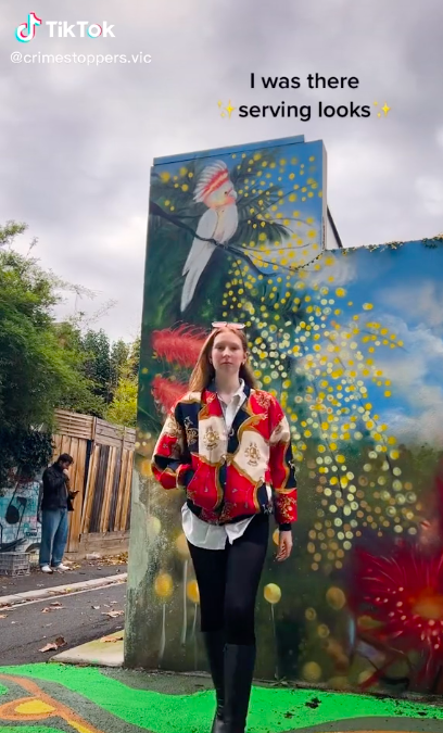 Screenshot of a TikTok of a girl walking towards camera wearing a bright jacket in front of a mural