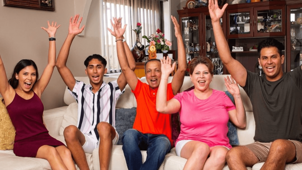 The Delpechitra family on Gogglebox Australia, sitting on the couch with their arms in the air celebrating