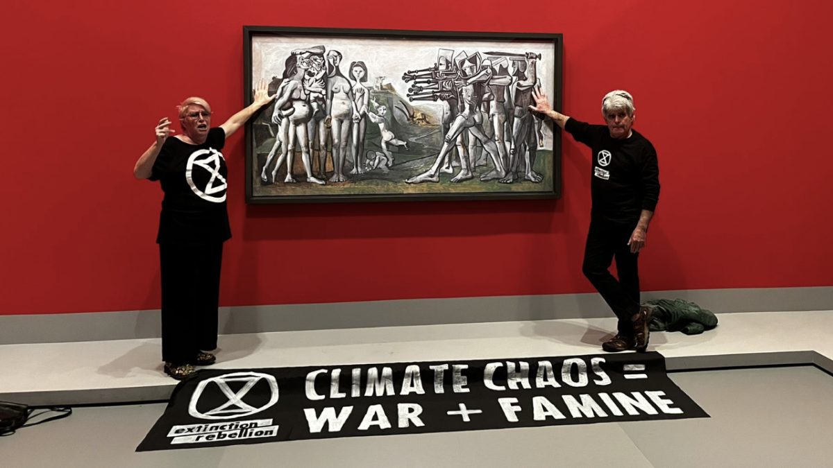 Two Extinction Rebellion protestors dressed in black glued to a Pablo PIcasso painting at the National Gallery of Victoria with a banner by their feet that reads "climate chaos = war and famine"