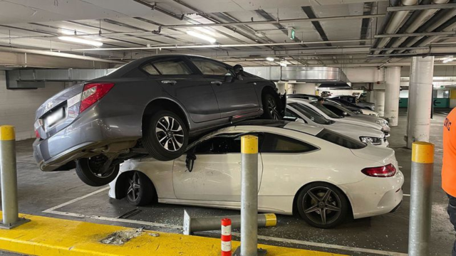 A grey Honda Civic that has driven on top of a white Mercedes-Benz at Westfield Hurstville in Sydney