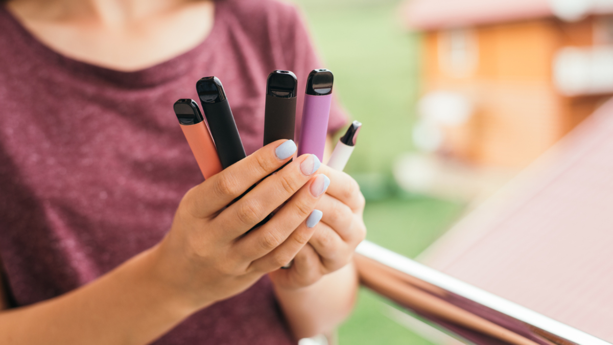 Girl in a purple t-shirt holding different coloured vape pens