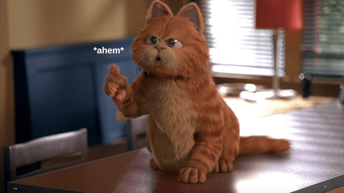 Garfield in movie sitting on a table holding paw up saying "ahem"