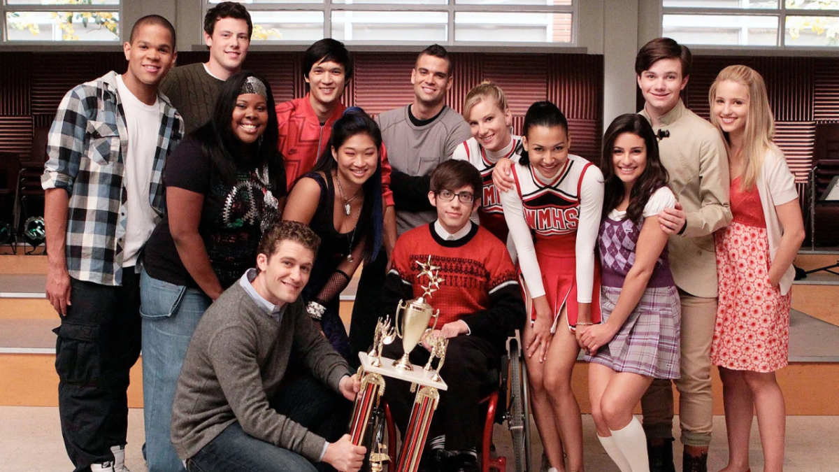Glee cast posing for photo on show in choir room.