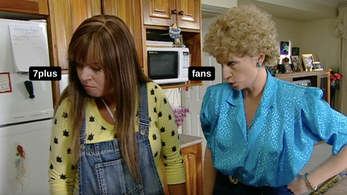 Kath & Kim - Kim wearing blue overalls and a yellow shirt and Kim scolding her wearing a blue shirt, both standing in kitchen