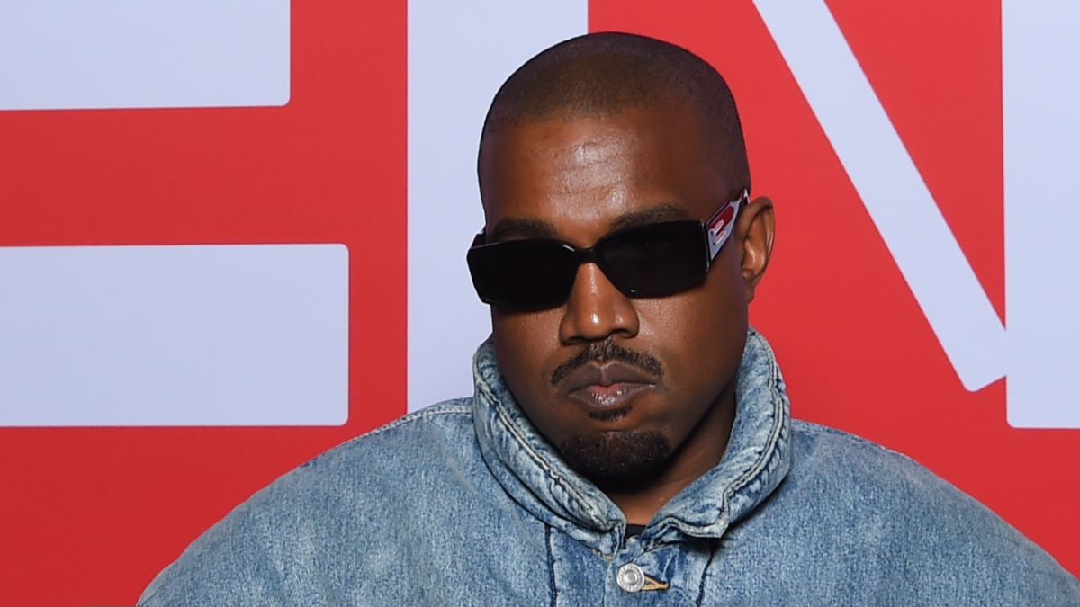 Kanye West attending Kenzo Fall/Winter 2022/2023 show wearing denim jacket and black sunglasses. The rapper may not be able to enter Australia due to past anti-Semitic comments.