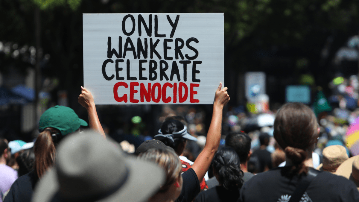 Protesters hold placards as they make their way towards Victoria Park during an Invasion Day protest. One protester is holding a sign which reads: Only wankers celebrate genocide