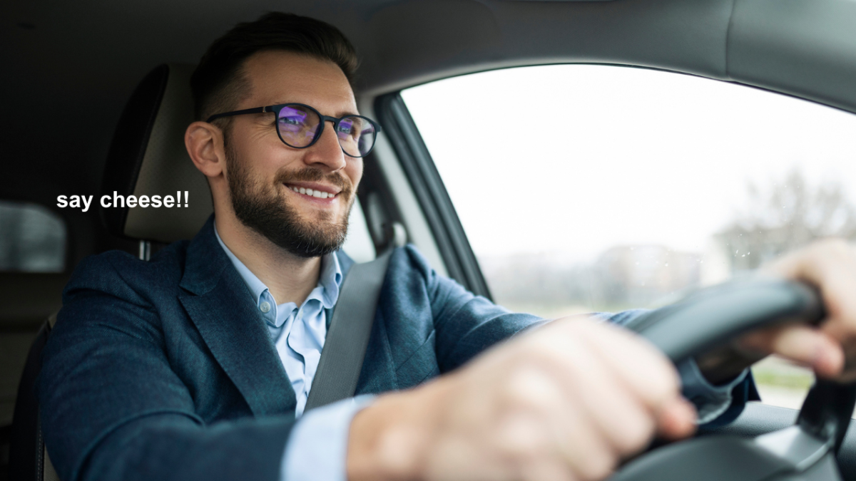 stock photo of man driving car with text which reads "say cheese!!"