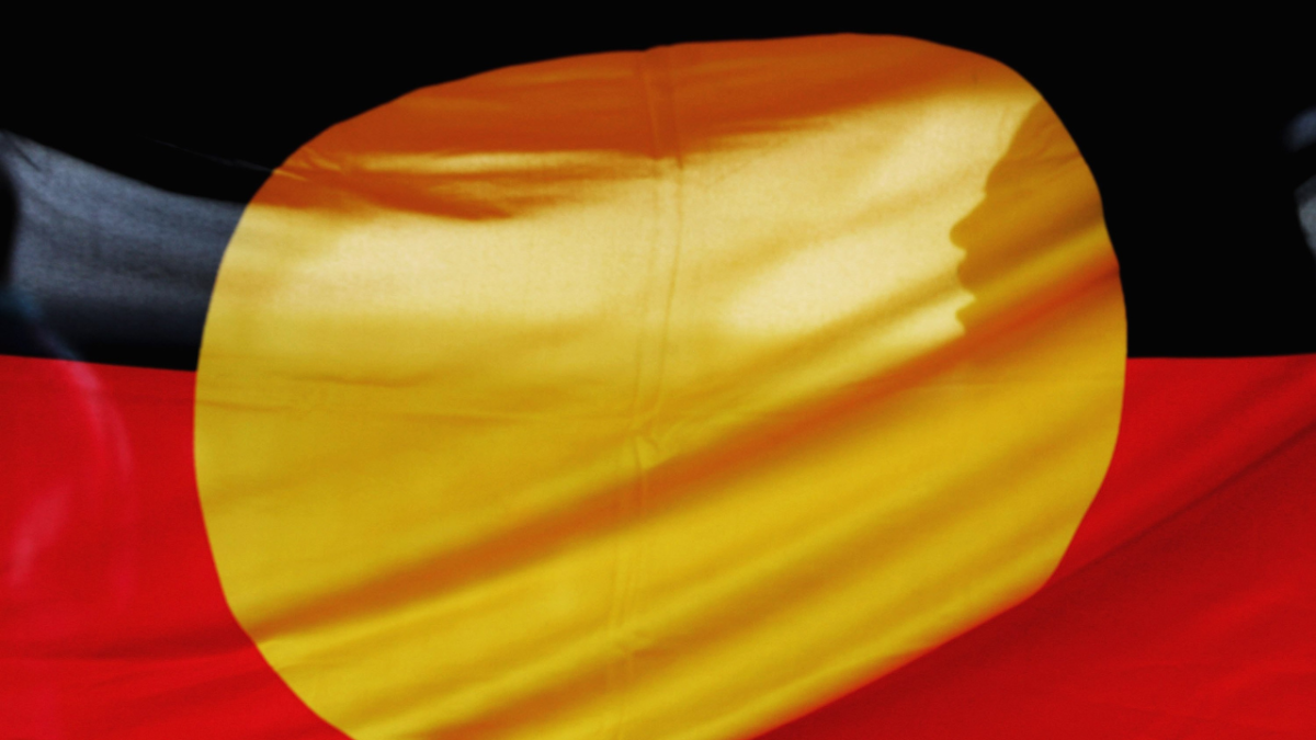 On the 25th anniversary of National Sorry Day the image is of an Indigenous Flag with a shadow of a face shining onto the flag