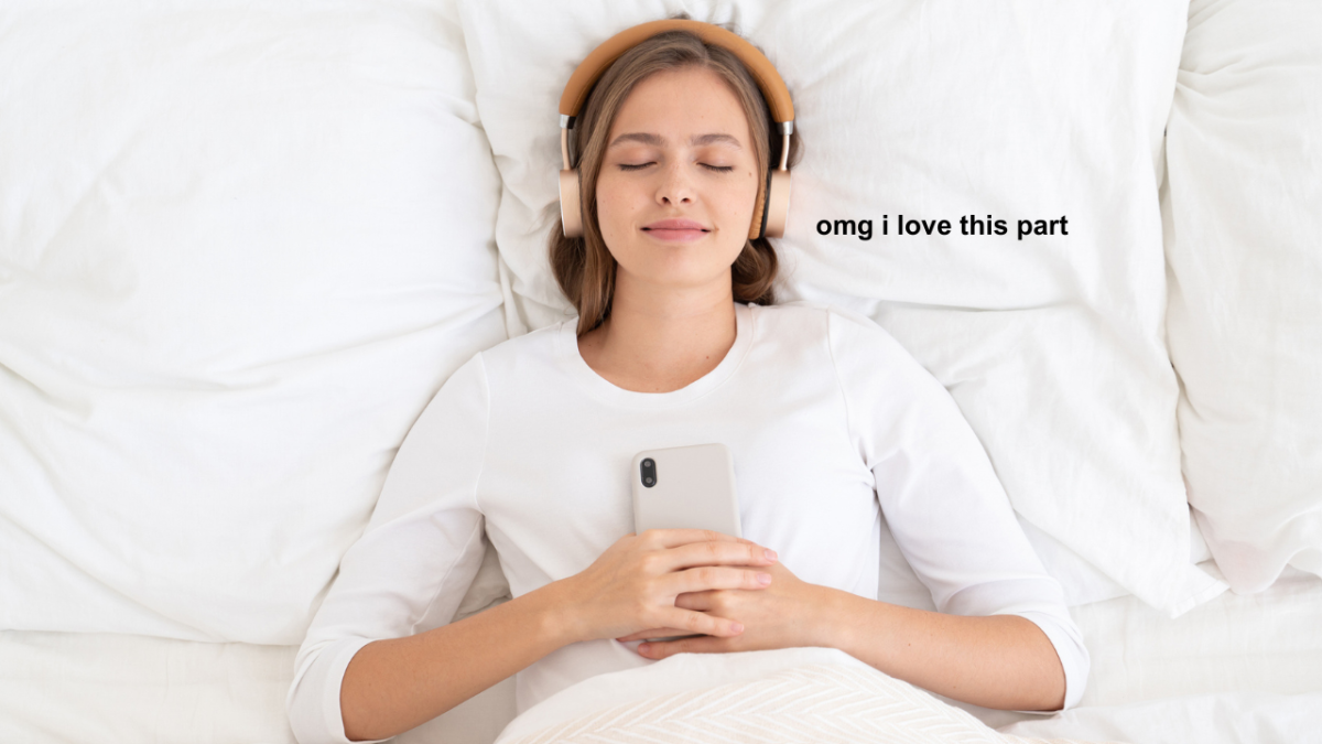 Stock image of woman in bed holding phone with headphones in and black text which reads "omg i love this part" after an expert revealed why some people find true crime relaxing