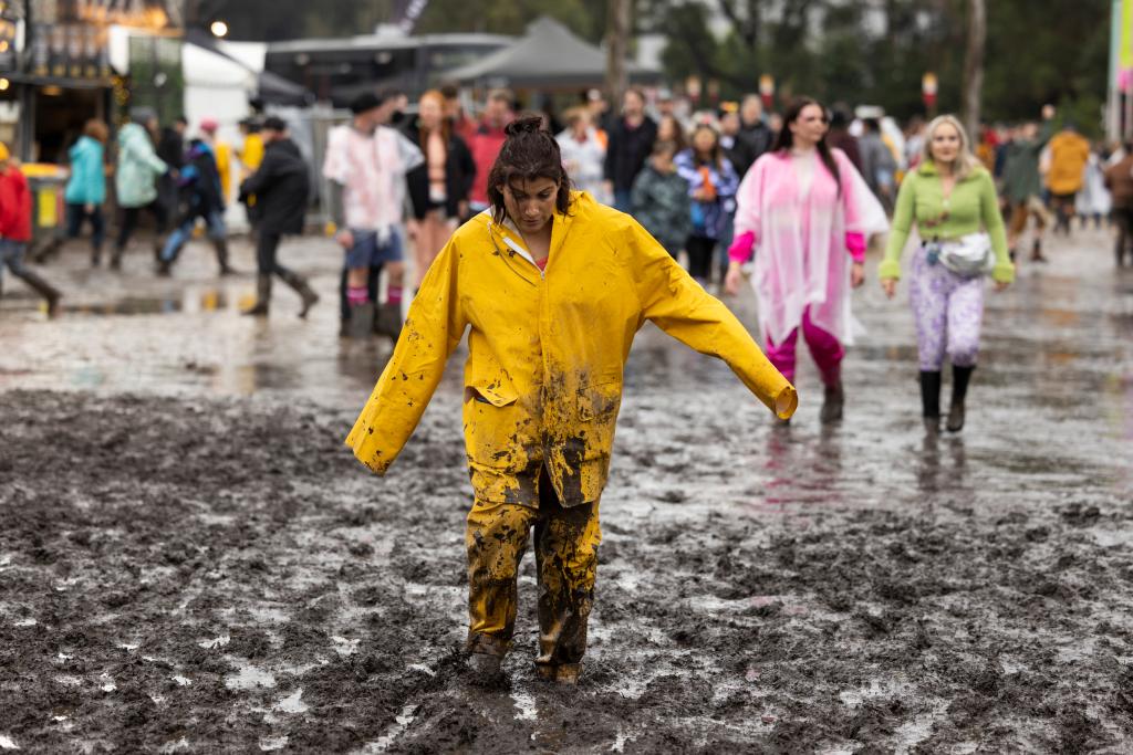 Woman walks through mud in yellow raincoat suit at Splendour in the Grass 2022