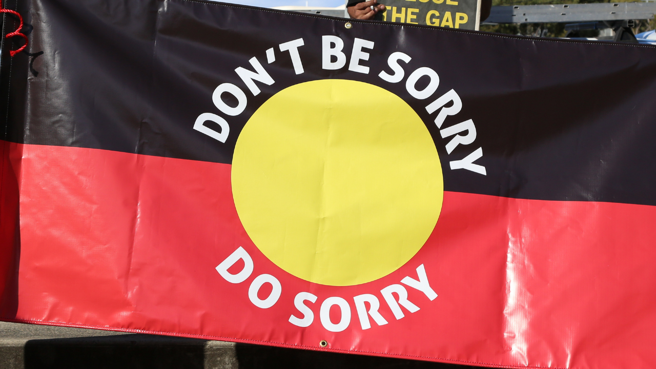 aboriginal flag that says "don't be sorry, do sorry" in response to increase of aboriginal children in foster care