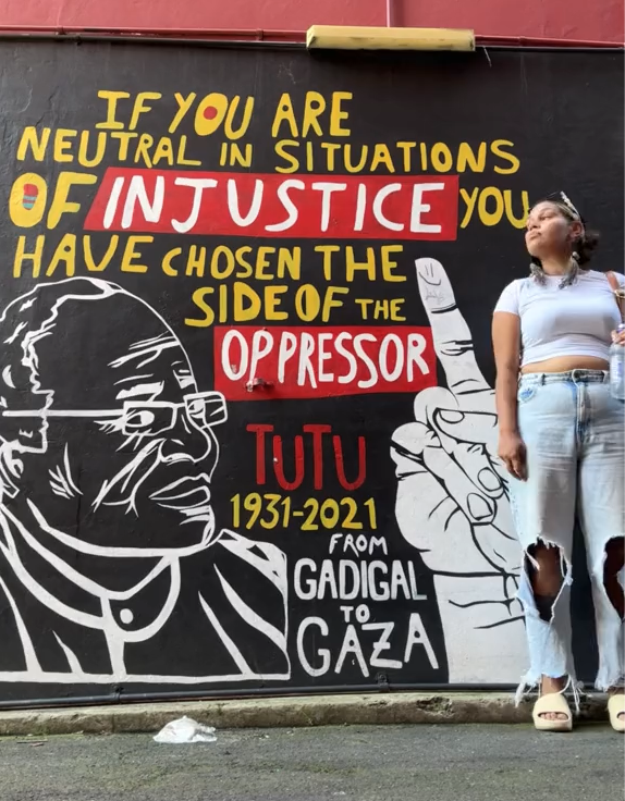 Barkaa standing in front of a mural that says if you are neutral in situations of injustice you have chosen the side of the opressor